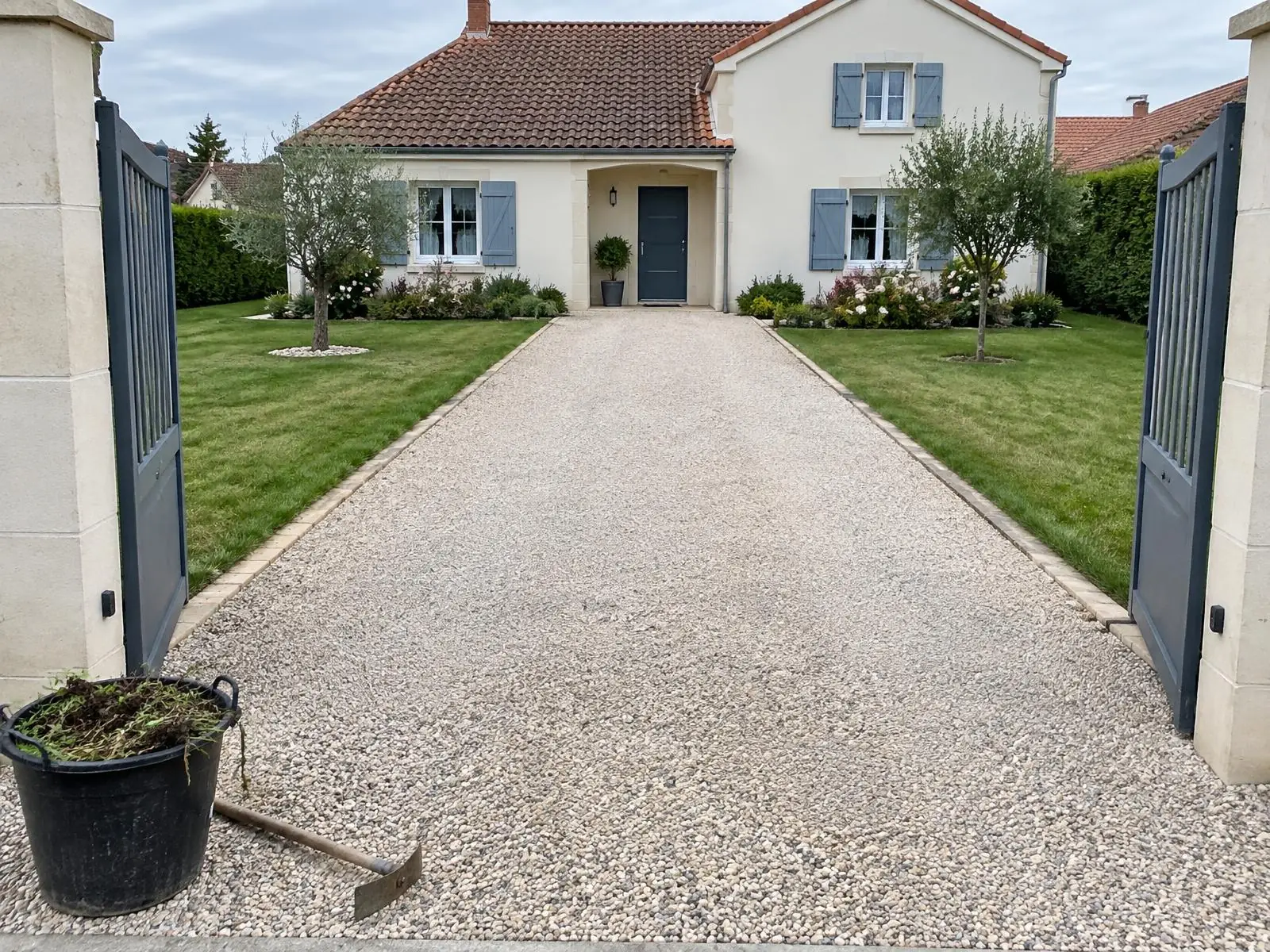La même allée désherbée et ratissée, pelouses tondues et bordées, seau d’herbes arrachées et binette à l’entrée